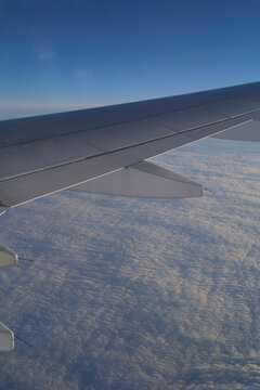 Wing of an airplane flying above a cloudscape at high altitude with clear blue sky in the background.