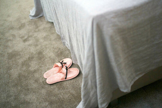 Pink slippers on a carpeted floor beside a bed with a white bedsheet, Vienna, Austria