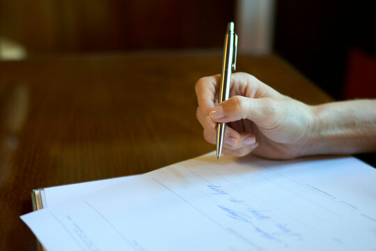 Close-up of a hand signing a document during a wedding ceremony with a gold pen on a wooden table, Dresden, Germany