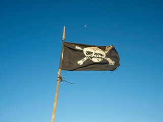 A pirate flag with a skull and crossbones flutters against a clear blue sky with a crescent moon, Fuerteventura, Spain