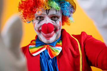 Happy clown in colorful costume against vibrant yellow background.