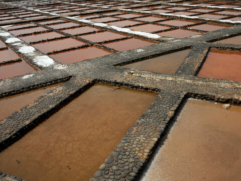 Aerial view of salt pans with water at various stages of evaporation framed by stone boundaries, Fuerteventura, Spain