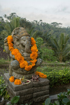 A decorated statue of Ganesha with orange marigold garlands and offerings with a lush green backdrop, Bali, Indonesia