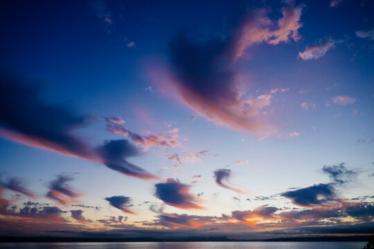 Sunset sky with streaks of pink and purple clouds over a tran0uil water body.