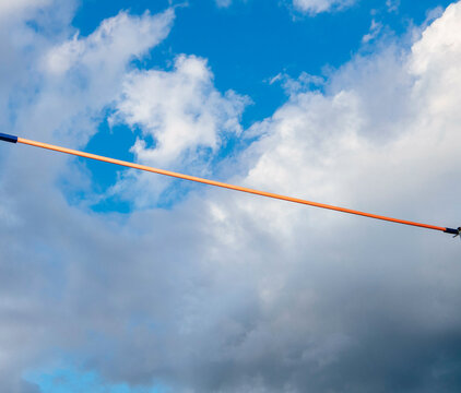 Orange horizontal pole vault against a backdrop of blue sky and fluffy white clouds.