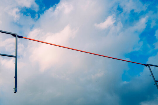 A red horizontal pole vault bar set against a cloudy blue sky during a high jump athletic event