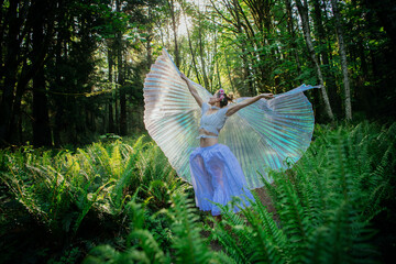 Woman in forest performing with large iridescent wings among ferns, USA