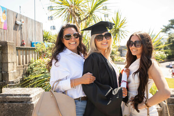 Three women celebrating graduation day with smiles and embracing in the sunshine, Bournemouth, Dorset UK