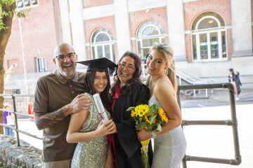 Smiling family celebrating a young woman's graduation outside a brick building with large windows, Bournemouth, Dorset UK