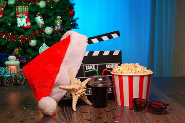 Merry Christmas and New Year Holidays Scene. Santa Claus Hat, Movie Clapperboard, Christmas Tree, Garland, Neon Lights, Cinema Popcorn, and 3D Glasses. Perfect Setting for Holiday Movie Nights at Home