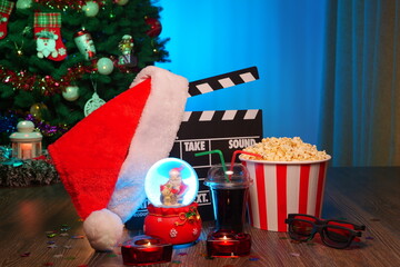 Merry Christmas and New Year Holidays Scene. Santa Claus Hat, Movie Clapperboard, Christmas Tree, Garland, Neon Lights, Cinema Popcorn, and 3D Glasses. Perfect Setting for Holiday Movie Nights at Home