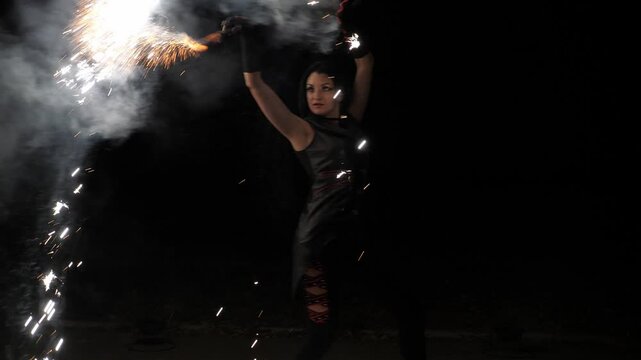 The artist of the fire show in black clothes throws fire sparks. An impressive beautiful performance with fire and fireworks. Slow motion. A professional circus performer dancing with fire.