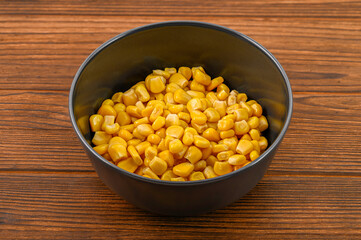 Close-up of vibrant yellow corn kernels in a sleek black clay bowl on a rustic wooden background, creating an appetizing and colorful presentation of this nutritious vegetable