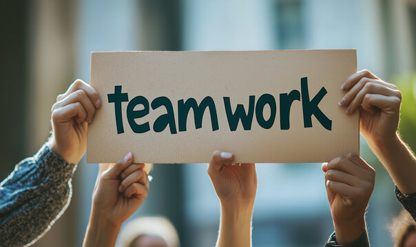 A diverse group of hands holding up a cardboard sign with the word "teamwork," symbolizing collaboration and unity against a blurred background