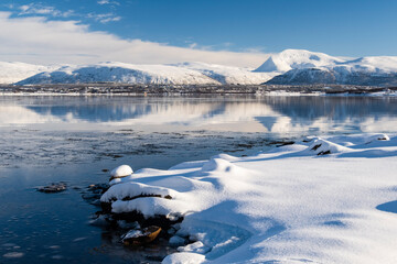 Snow covered coast of Norwegian fjord near Troms at Christmas time. A sunny winter day in Northern Norway above the Arctic Circle