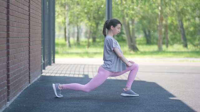 A girl in a T-shirt and a pink bodysuit is warming upA girl in a T-shirt and a pink bodysuit is warming up