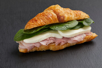 Delicious croissant with ham , mozzarella cheese and spinach on black background