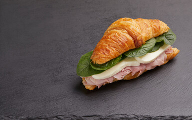 Delicious croissant with ham , mozzarella cheese and spinach on black background
