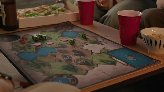 Closeup of tattooed guy rolling dice on table while playing boardgame with friends in cozy home setting
