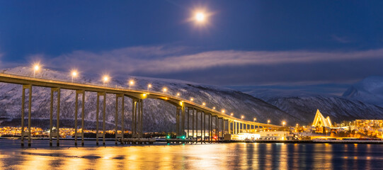 Panorama of the Norwegian city of Tromso on a winter evening during the Christmas season. The bridge over the fjord and houses are illuminated by city lights