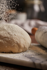 Cooking homemade bread. Sieving flour over raw bread dough rolled with rolling pin on marble board, dark background, selective focus. Baker hands on dough.