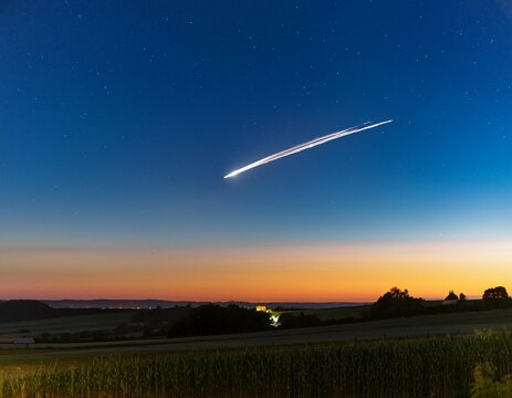 une comete traverse le ciel dans un paysage de campagne tres tot le matin