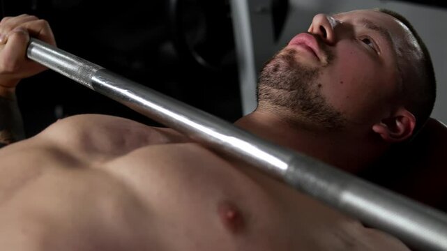 A close-up of a young athletic man doing a barbell bench press exercise lying in a Smith simulator, a man without a T-shirt demonstrates his pumped chest muscles.