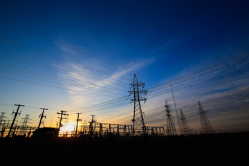 Many high-voltage power towers, silhouetted against the setting sun