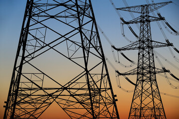 Many high-voltage power towers, silhouetted against the setting sun
