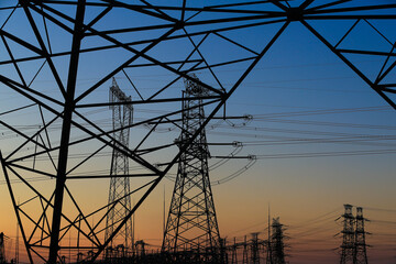 Many high-voltage power towers, silhouetted against the setting sun