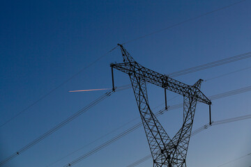Many high-voltage power towers, silhouetted against the setting sun