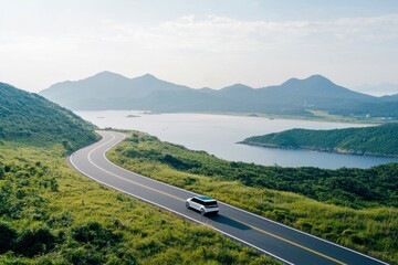 Obraz premium A scenic road winds through lush hills beside a serene lake and mountains, with a car traveling along the picturesque route.