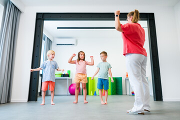 Fototapeta premium Young children exercising with physical therapist during group therapy session. Child occupational physical therapy. Bilateral coordination.