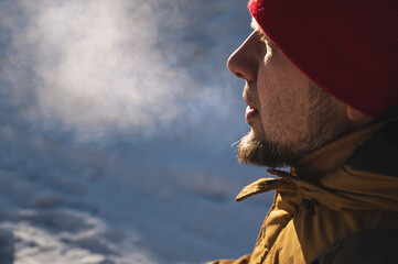 Bearded man in red hat in inhales frosty air and exhales steam.  breathe out steam outdoor in winter