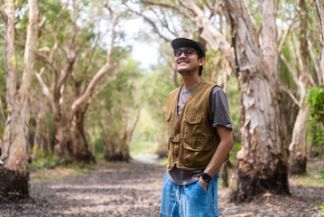 Happy asian man smiling in mangrove forests. He admires lush foliage, serene ambiance in tropical botanical garden. Traveler enjoys eco-tourism, nature walks.