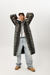 Confidently posing, a fashionable man showcases his striking leopard print coat in a studio.