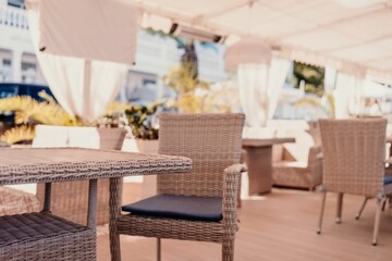 Wicker furniture tables in the open air are waiting for visitors. The interior of the restaurant in the open air. Empty tables of street cafe.
