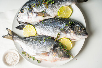 Three raw fish dorado with lime and lemon with herbs and salt and pepper on a white plate on a light table