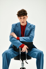 Handsome man sits on chair, showcasing trendy attire with relaxed yet focused demeanor