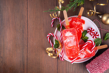 Festive Christmas holiday sweet mint candy cane peppermint popsicles ice cream, frozen creamy red and white yogurt sorbet lollypops, on Christmas New Year decorated background, copy space