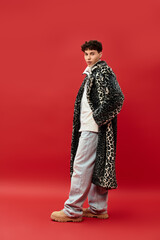 Confident man showcases unique fashion in a leopard print coat with a striking red backdrop.