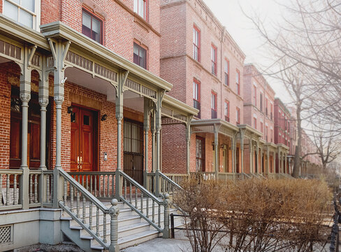 Row of brick buildings. The buildings have a classic old-fashioned look. The porch is decorated with wooden railings. Harlem Houses in New York City. House on Astor Row.