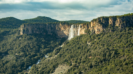 Scenic view of a waterfall flowing down a rocky cliff surrounded by a dense forest, creating a breathtaking natural landscape