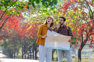 Naklejka premium young caucasian couple traveling in autumn park,they are looking at a paper map for direction