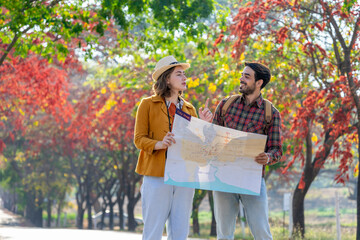 Naklejka premium young caucasian couple traveling in autumn park,they are looking at a paper map for direction