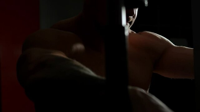 A close-up silhouette of a man doing strength exercises in the gym, performing exercises for the pectoral muscles on the pec deck simulator. A bodybuilder trains in a dark gym.