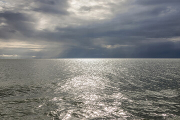 The IJsselmeer lake in the Netherlands from the ferry, with sunlight breaking through dark clouds and reflecting on calm water.