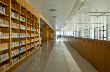 Interior view of a modern library with wooden bookshelves neatly organized with books, a polished floor in the hallway. A clean, minimalistic space for reading, studying, or research.