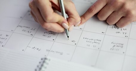 An individual diligently writing on a calendar to effectively manage their daily schedule and appointments