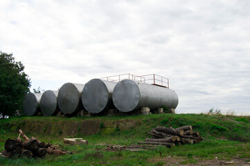 Large metal industrial tanks sit in an overgrowing area.